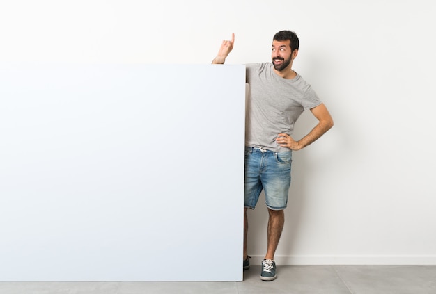 Jonge knappe man met baard met een groot blauw leeg bordje van plan om de oplossing te realiseren terwijl hij een vinger opheft