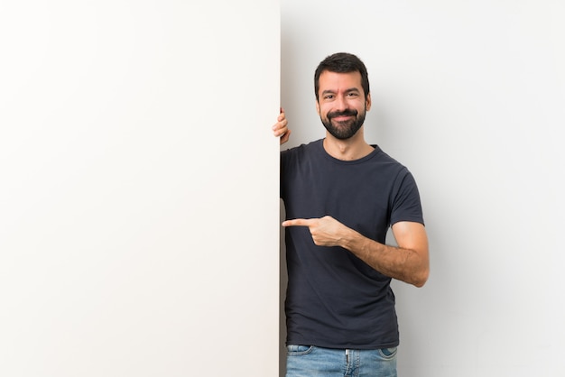 Jonge knappe man met baard met een groot leeg bordje wijzende vinger naar de kant