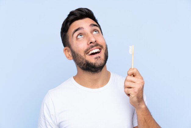 Jonge knappe man met baard zijn tanden poetsen over geïsoleerde muur te kijken terwijl het glimlachen