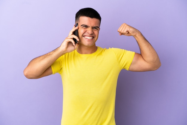 Jonge knappe man met behulp van mobiele telefoon over geïsoleerde paarse achtergrond doet sterk gebaar