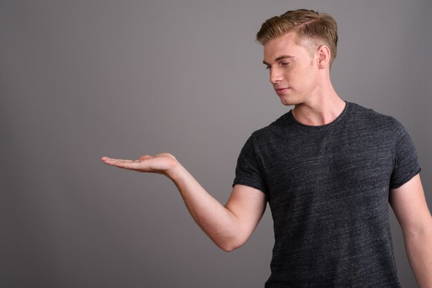 Jonge knappe man met blond haar grijs shirt dragen op grijze muur