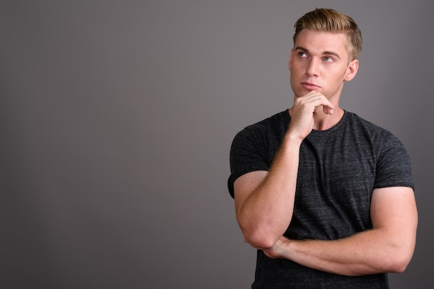 Jonge knappe man met blond haar grijs shirt dragen op grijze muur