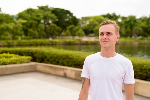 Jonge knappe man met blond haar ontspannen in het park