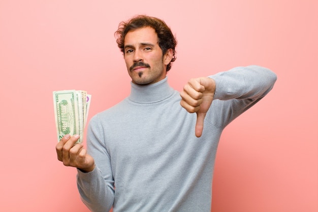 Jonge knappe man met dollarbankbiljetten op roze muur