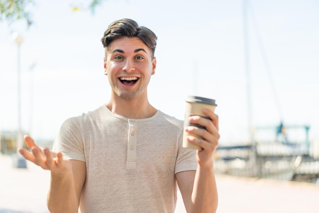 Jonge knappe man met een afhaalkoffie buitenshuis met geschokte gezichtsuitdrukking