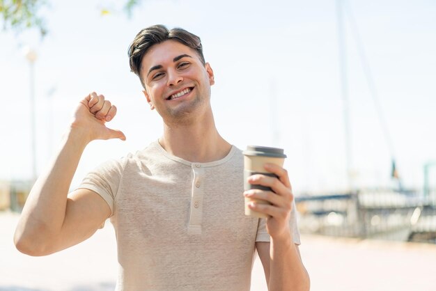 Jonge knappe man met een afhaalkoffie buitenshuis trots en zelfvoldaan