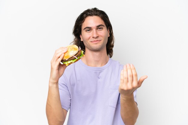 Jonge knappe man met een hamburger geïsoleerd op een witte achtergrond die uitnodigt om met de hand te komen Blij dat je gekomen bent
