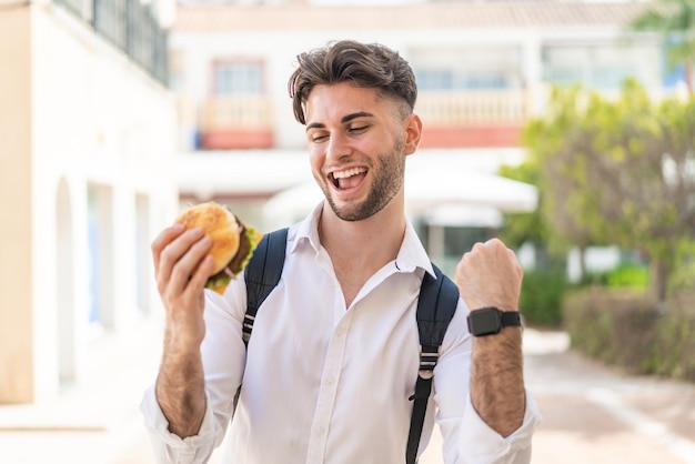 Jonge knappe man met een hamburger in de open lucht om een overwinning te vieren