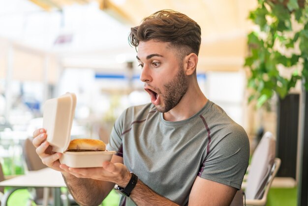 Jonge knappe man met een hamburger met verbaasde uitdrukking