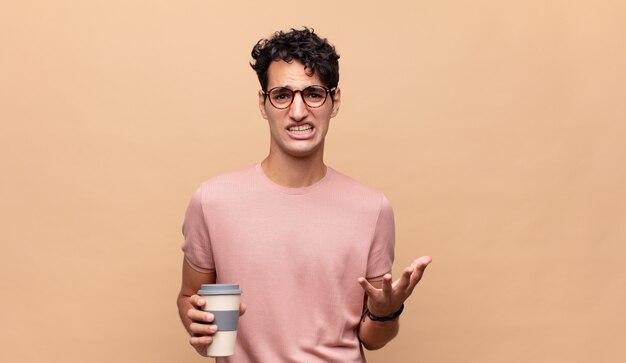 Jonge knappe man met een kopje koffie op zoek wanhopig en gefrustreerd