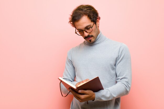 Jonge knappe man met een notitieboek tegen roze platte muur