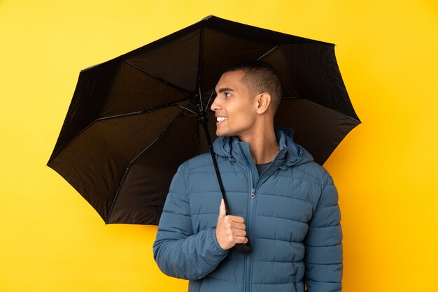 Jonge knappe man met een paraplu over geïsoleerde gele muur met gelukkige uitdrukking