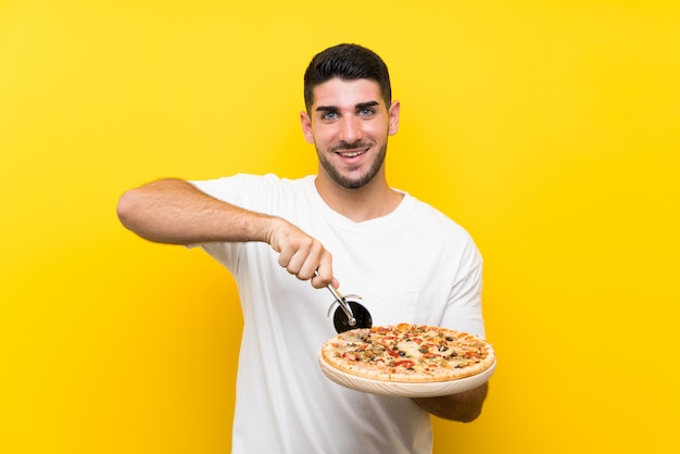 Jonge knappe man met een pizza over geïsoleerde gele muur