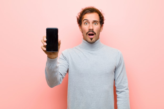 Jonge knappe man met een slimme telefoon op roze platte muur