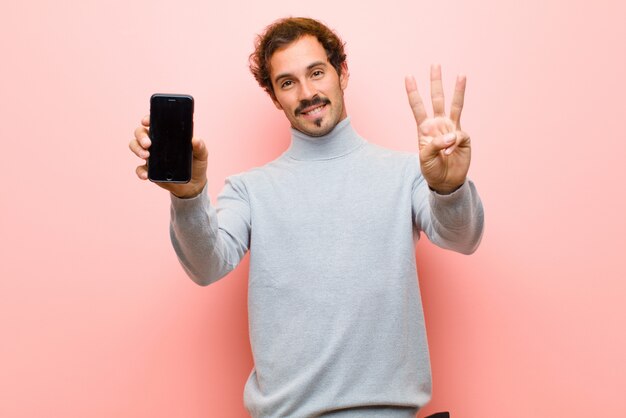 Jonge knappe man met een slimme telefoon tegen roze platte muur