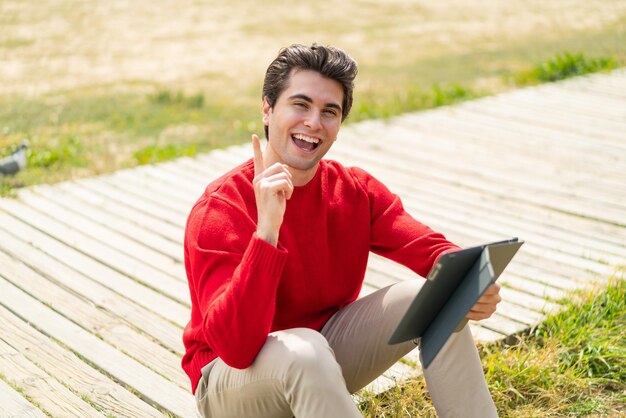 Jonge knappe man met een tablet buitenshuis die een geweldig idee benadrukt