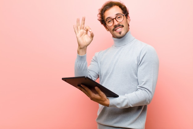 Jonge knappe man met een tablet tegen roze platte muur