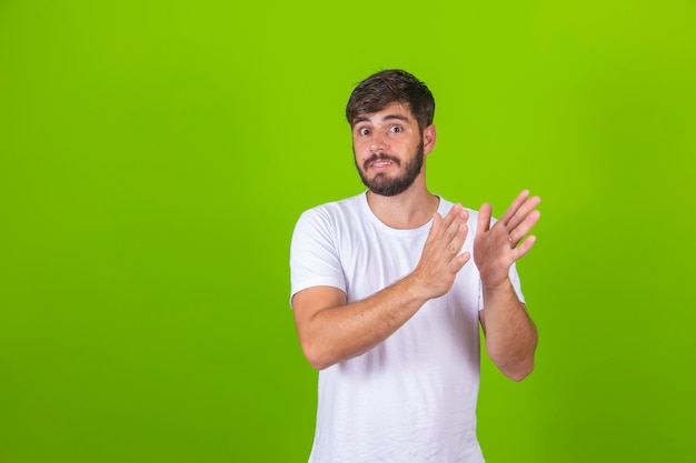 Jonge knappe man met een wit t-shirt die over een geïsoleerde groene achtergrond staat te klappen en te applaudisseren, gelukkige en vrolijke lachende trotse handen samen