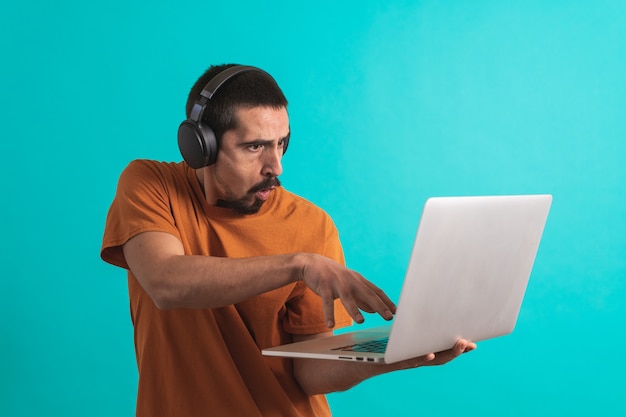 Jonge knappe man met gamer hoofdtelefoon set geïsoleerd op blauwe achtergrond met behulp van laptop
