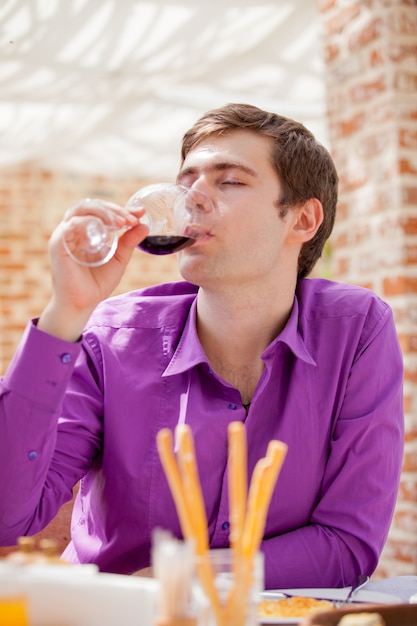 Jonge knappe man met glas wijn in restaurant in de zomer.