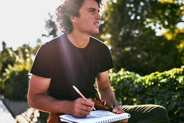 Jonge knappe man met krullend haar die enkele mededelingen op papier schrijft en zich voorbereidt op examen zittend op de straat van de stad Freelancer zakenman maakt plannen voor nieuwe projecten