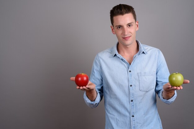 jonge knappe man met rode appel en groene appel op grijs