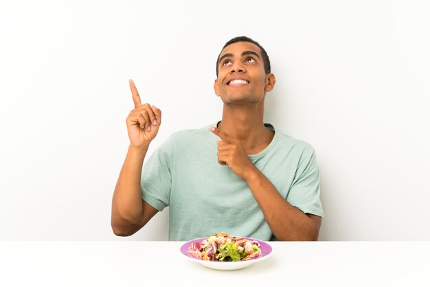 Jonge knappe man met salade in een tabel wijzend met de wijsvinger een geweldig idee