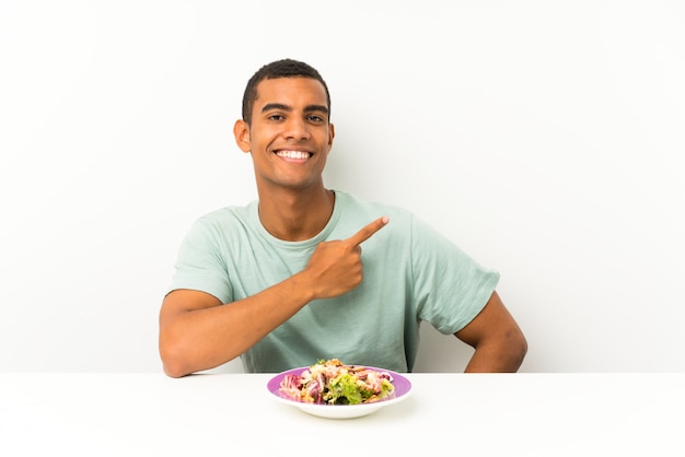 Jonge knappe man met salade in een tafel wijzende vinger aan de zijkant