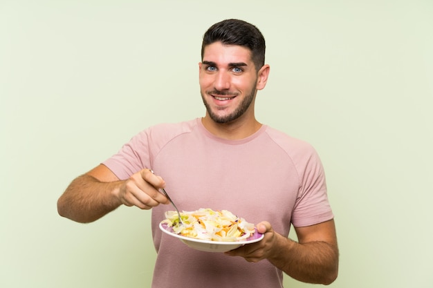 Jonge knappe man met salade over geïsoleerde groene muur