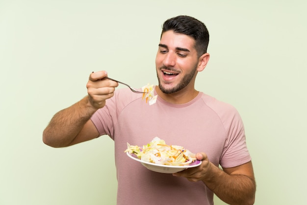 Jonge knappe man met salade over geïsoleerde groene muur