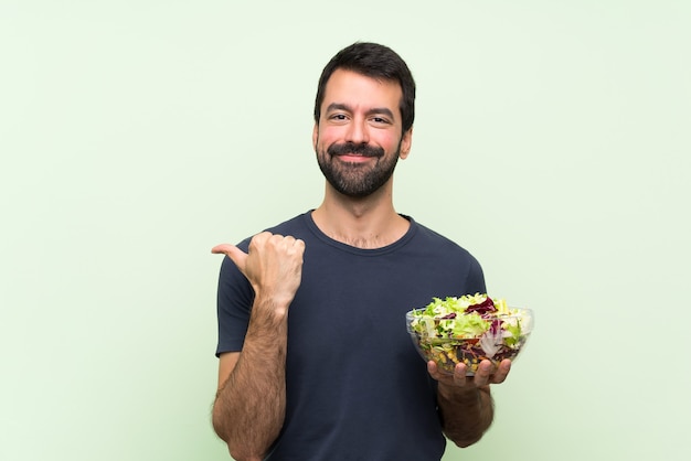 Jonge knappe man met salade wijst naar de zijkant om een product te presenteren