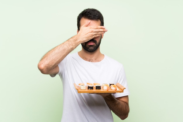 Jonge knappe man met sushi die ogen behandelen door handen