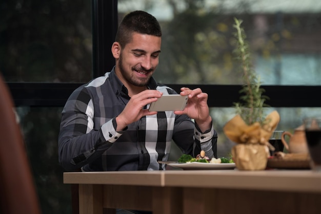 Jonge knappe man nemen foto van Appertizer met Smartphone Camera in Restaurant