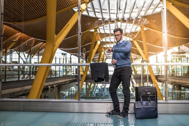 Jonge knappe man ongelukkig boos op de luchthaven wachten zijn vertraagde vlucht met bagage