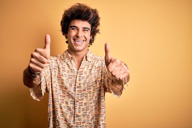 Jonge knappe man op vakantie zomer shirt dragen over geïsoleerde gele achtergrond goedkeuren doen positief gebaar met hand duimen omhoog glimlachen en blij voor succes Winnaar gebaar