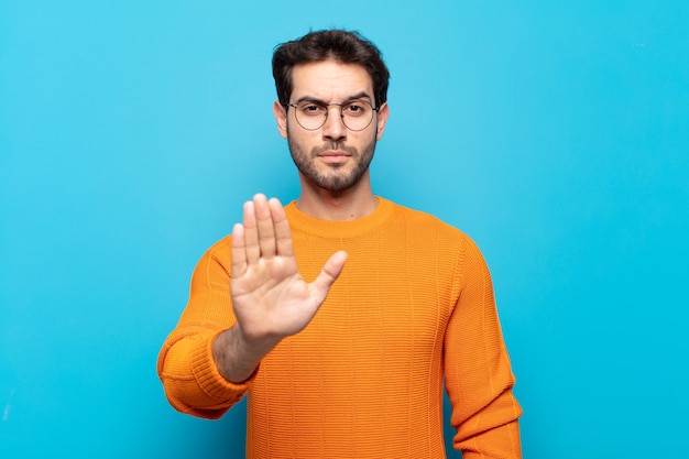 Foto jonge knappe man op zoek ernstig, streng, ontevreden en boos met open palm stop gebaar maken