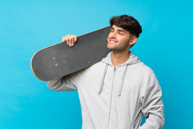 Jonge knappe man over geïsoleerde blauw met skate en op zoek kant