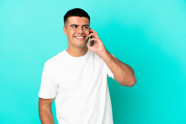 Jonge knappe man over geïsoleerde blauwe achtergrond die een gesprek voert met de mobiele telefoon met iemand