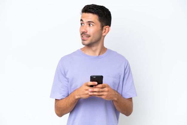 Jonge knappe man over geïsoleerde witte achtergrond die mobiele telefoon gebruikt en omhoog kijkt