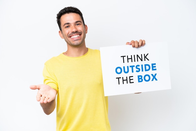 Jonge knappe man over geïsoleerde witte achtergrond met een bordje met de tekst Think Outside The Box die een deal sluit