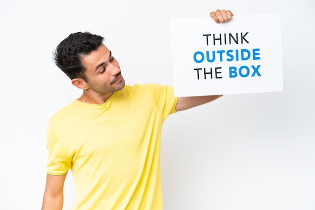 Jonge knappe man over geïsoleerde witte achtergrond met een bordje met tekst Think Outside The Box