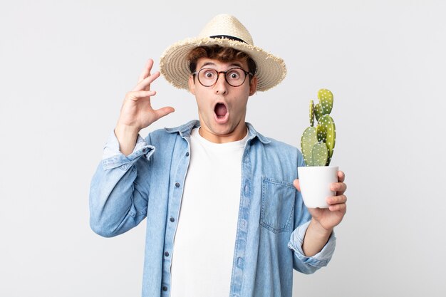 Jonge knappe man schreeuwen met handen omhoog in de lucht. boer met een decoratieve cactus