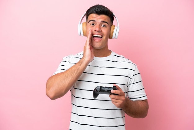 Jonge knappe man speelt met een videogamecontroller geïsoleerd op een roze achtergrond met verrassing en geschokte gezichtsuitdrukking