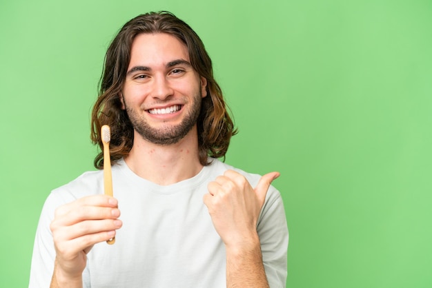 Jonge knappe man tandenpoetsen over geïsoleerde achtergrond wijzend naar de zijkant om een product te presenteren