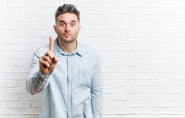 Jonge knappe man tegen een bakstenen muur met nummer één met vinger.