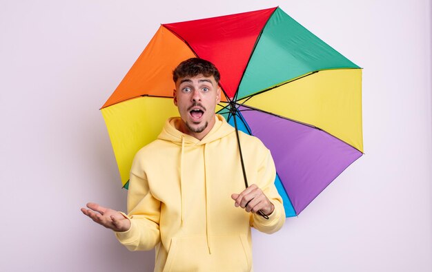 Jonge knappe man verbaasd, geschokt en verbaasd met een ongelooflijke verrassing. paraplu concept