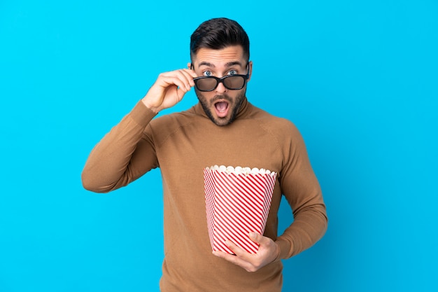 Jonge knappe man verrast met 3d bril en houden een grote emmer popcorns