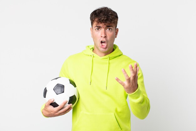 Jonge knappe man voelt zich extreem geschokt en verrast en houdt een voetbal vast