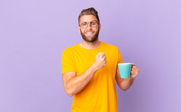 Jonge knappe man voelt zich gelukkig en staat voor een uitdaging of feest. en een koffiemok vasthouden