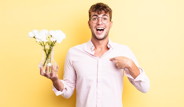 Jonge knappe man voelt zich gelukkig en wijst naar zichzelf met een opgewonden bloemen concept